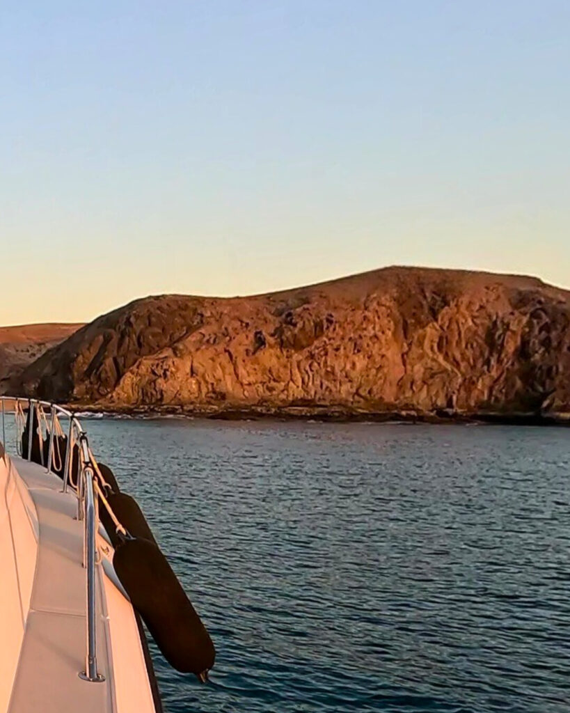 Vista lateral del yate privado navegando frente a los acantilados de Papagayo al atardecer.
